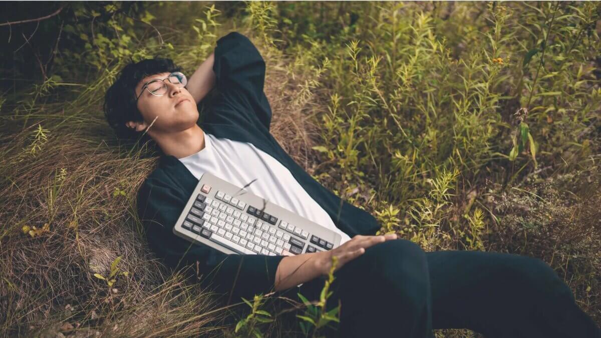 A man in repose amid the wildflowers of a meadow, lost in reverie, cradling his $3600 keyboard under his arm, thinking about the Stoics